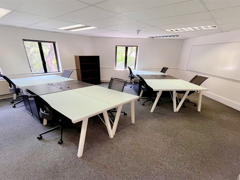 A functional office space featuring a suspended ceiling, recessed lighting, wall-mounted whiteboard, and carpeted flooring, providing a professional work environment.