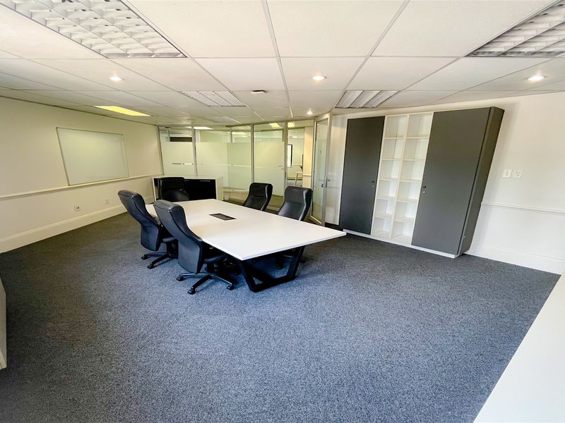 A professional office meeting room featuring a suspended ceiling, recessed lighting, built-in storage cabinetry, and a glass partition wall.