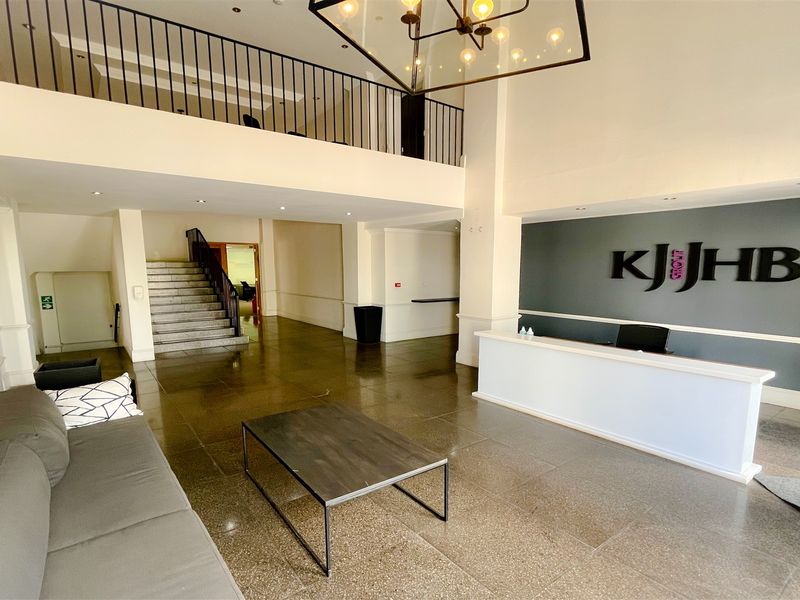 Spacious office reception area featuring a double-volume ceiling, mezzanine level with iron railing, stone flooring, and a built-in reception desk.