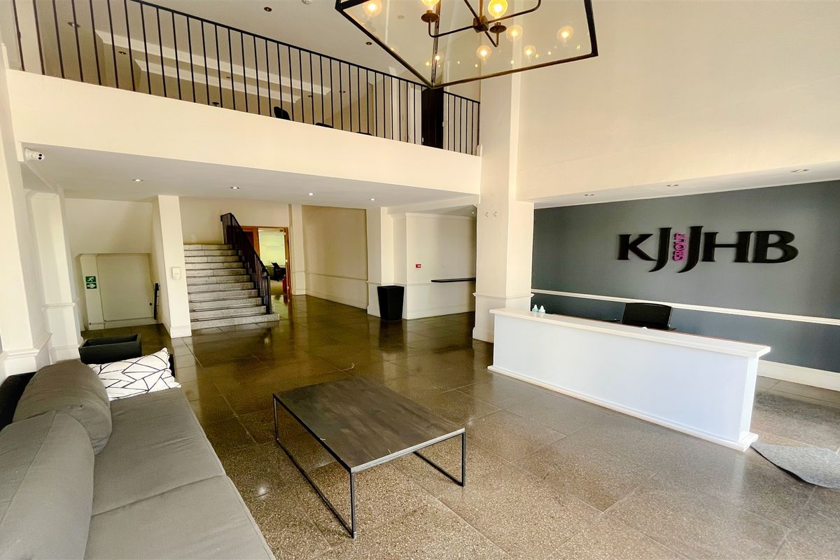 Spacious office reception area featuring a double-volume ceiling, mezzanine level with iron railing, stone flooring, and a built-in reception desk.