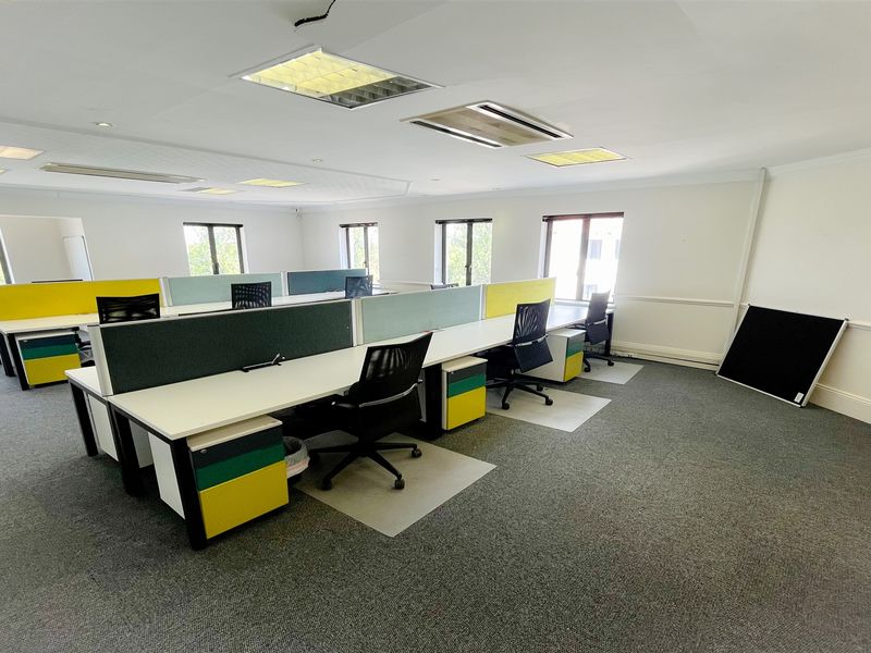 A spacious, well-lit open-plan office area featuring carpeted flooring, recessed ceiling lights, and integrated air conditioning units.