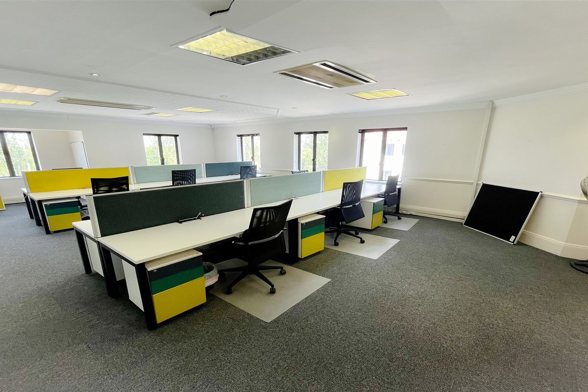 A spacious, well-lit open-plan office area featuring carpeted flooring, recessed ceiling lights, and integrated air conditioning units.