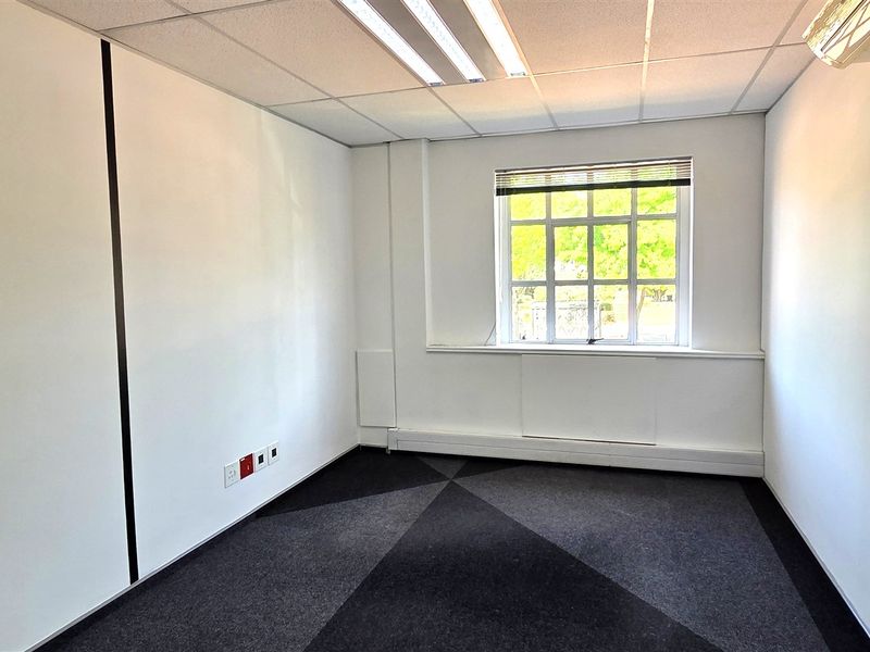 A clean, empty office space featuring carpeted flooring, a suspended ceiling with integrated lighting, and an air conditioning unit.
