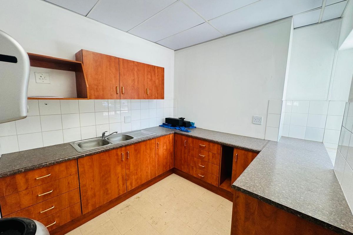 A functional office kitchenette featuring wood-look laminate cabinetry, a double stainless steel sink, tiled backsplash, and durable laminate countertops.