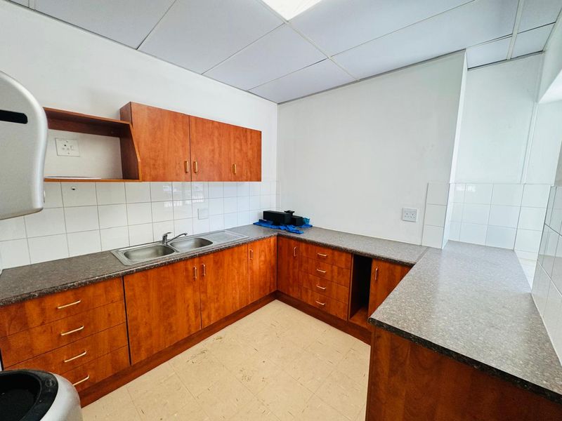 A functional office kitchenette featuring wood-look laminate cabinetry, a double stainless steel sink, tiled backsplash, and durable laminate countertops.