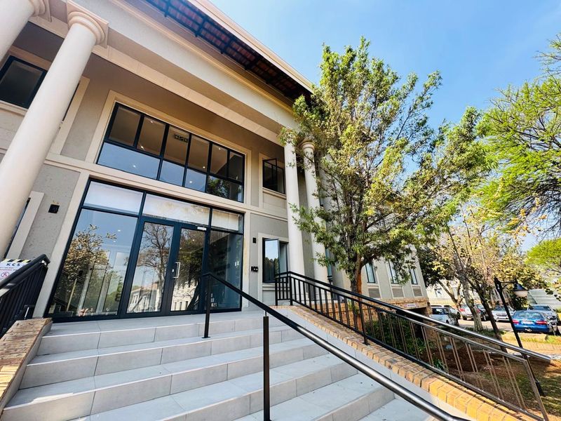 Front exterior view of a modern office building featuring a tiled entrance staircase, glass facade, and structural columns.