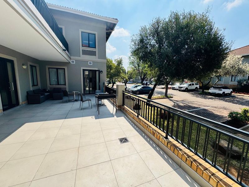 A spacious, well-maintained tiled patio area featuring a metal safety railing and brick base, overlooking the office complex parking area.