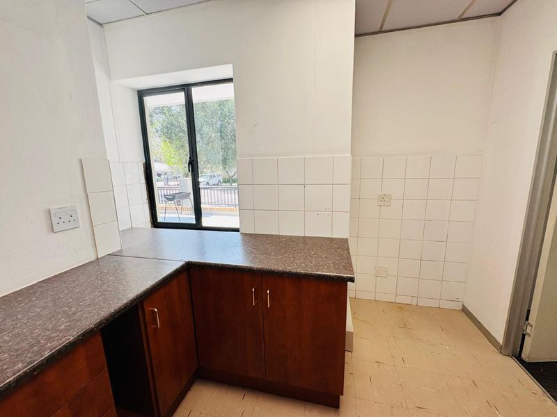A compact, empty kitchenette featuring wooden cabinetry, laminate countertops, and tiled splashbacks, suitable for office staff use.
