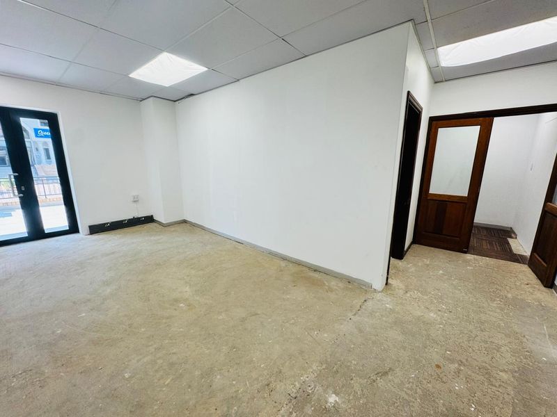 An empty office space featuring a suspended ceiling, recessed lighting, and direct access to an outdoor area through double glass doors.