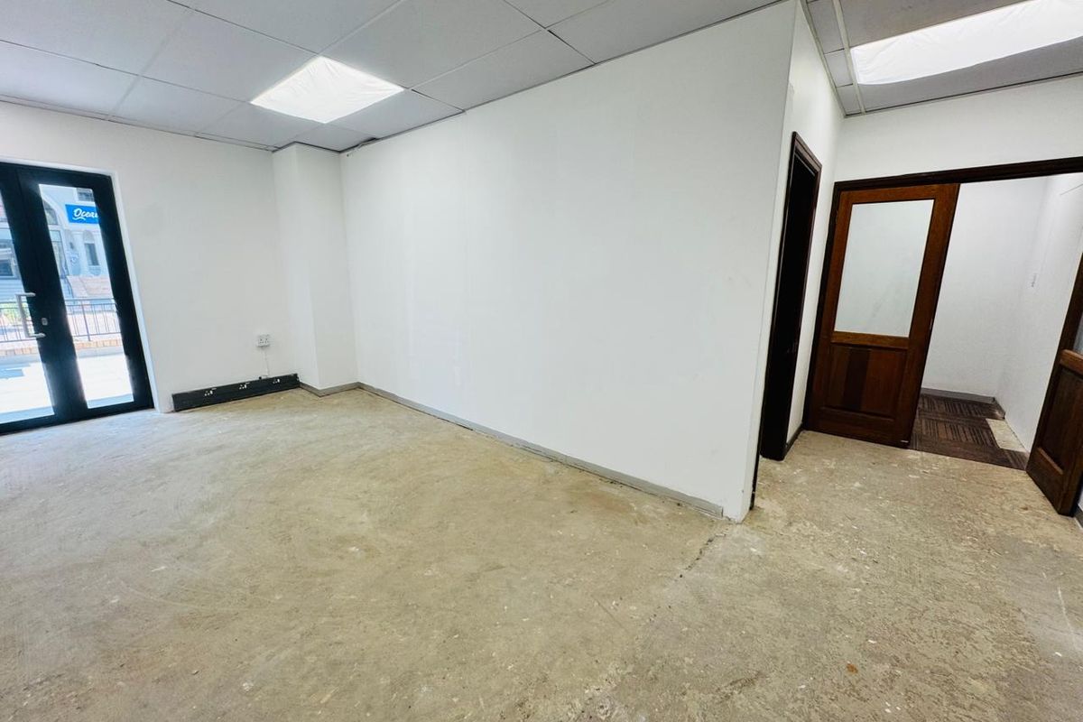An empty office space featuring a suspended ceiling, recessed lighting, and direct access to an outdoor area through double glass doors.