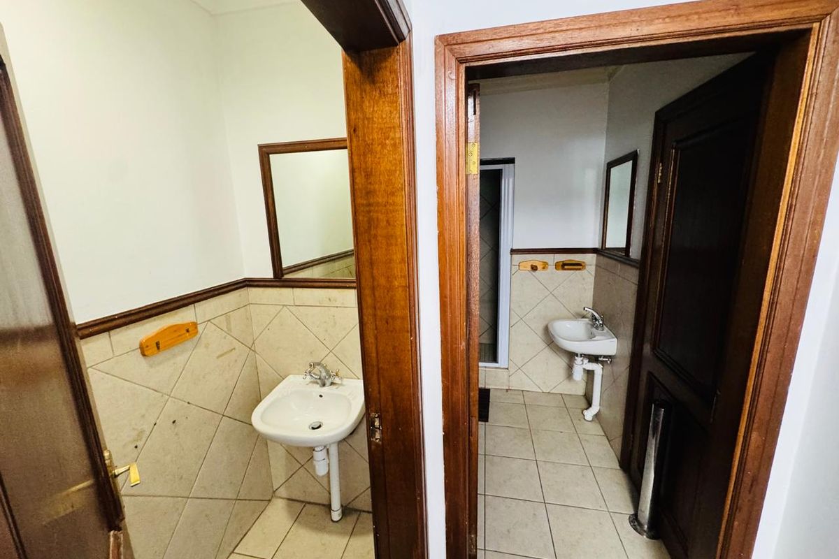 A functional office bathroom area featuring two separate washbasins with tiled splashbacks and classic wooden door frames.