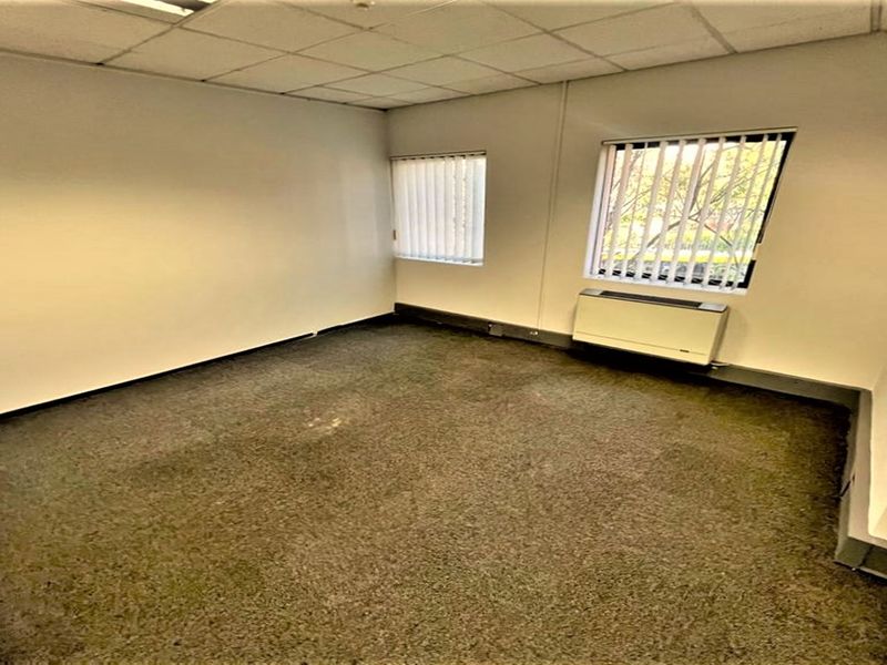An empty office space featuring a suspended ceiling, carpeted flooring, and vertical blinds on the windows.