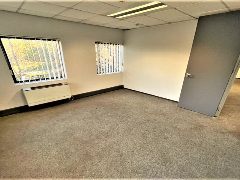 A vacant office space featuring a suspended ceiling, recessed lighting, vertical blinds, and an integrated HVAC unit with carpeted flooring.