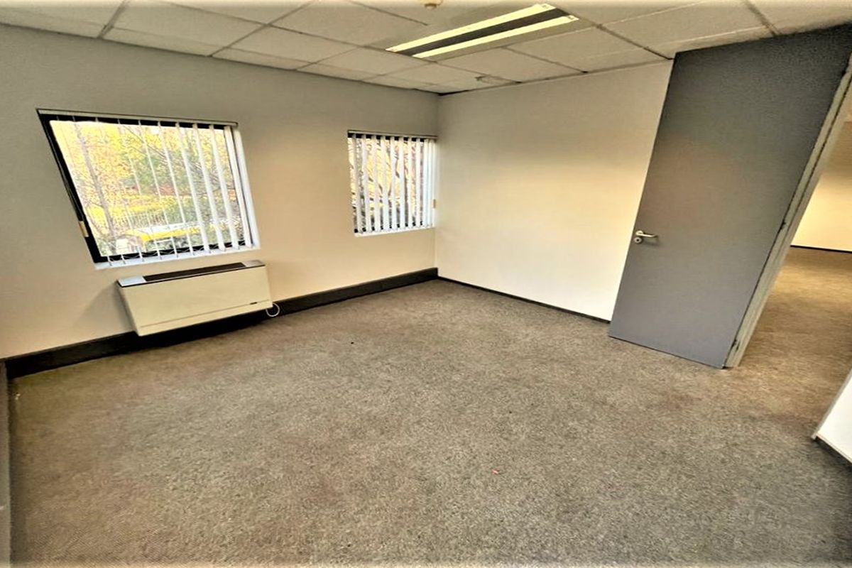 A vacant office space featuring a suspended ceiling, recessed lighting, vertical blinds, and an integrated HVAC unit with carpeted flooring.