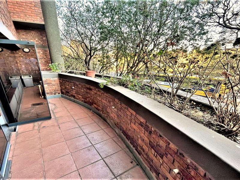 A private balcony featuring tiled flooring, a brick parapet wall, and direct access to the office interior through a glass sliding door.