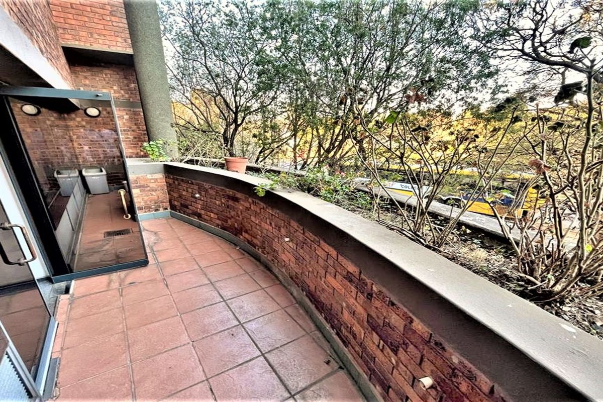A private balcony featuring tiled flooring, a brick parapet wall, and direct access to the office interior through a glass sliding door.