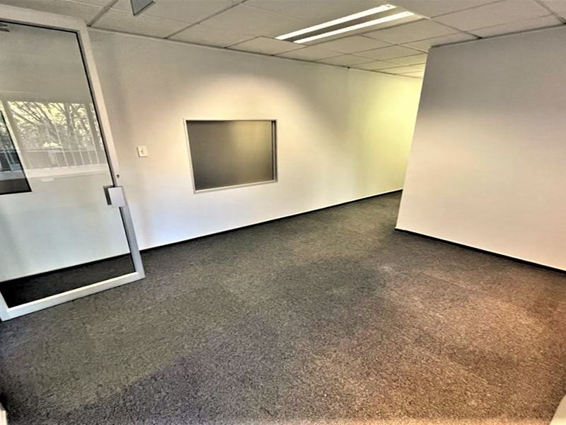 An empty office space featuring carpeted flooring, a suspended ceiling with recessed lighting, and a glass partition door.