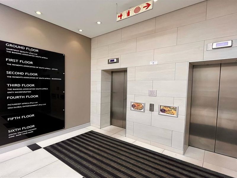 Modern office building lobby featuring stainless steel elevator banks, clear floor directory signage, and contemporary tiled finishes.