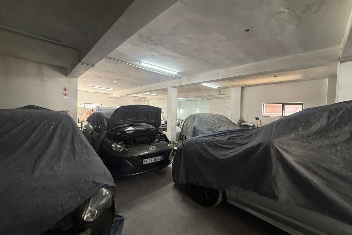 Spacious industrial garage area featuring concrete flooring, exposed structural columns, and fluorescent lighting, suitable for vehicle storage or workshop use.