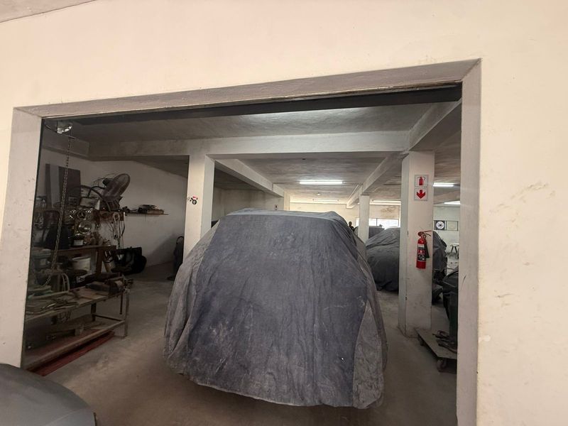 Spacious industrial garage or workshop area featuring concrete structural columns, overhead lighting, and fire safety equipment.