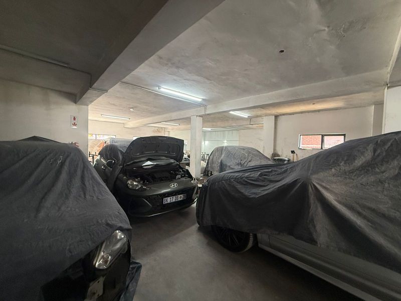 Spacious industrial garage area featuring concrete flooring, exposed structural columns, and fluorescent lighting, suitable for vehicle storage or workshop use.