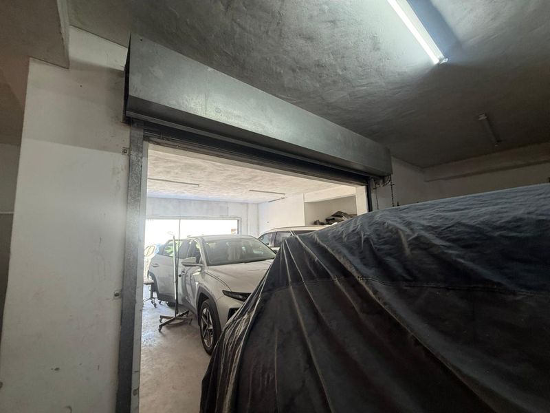 Industrial garage space featuring a metal roller shutter door, concrete flooring, and fluorescent lighting, suitable for vehicle storage or workshop use.