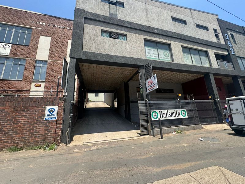 Industrial property facade featuring a concrete driveway entrance, multi-level structure with signage, and secure perimeter fencing.
