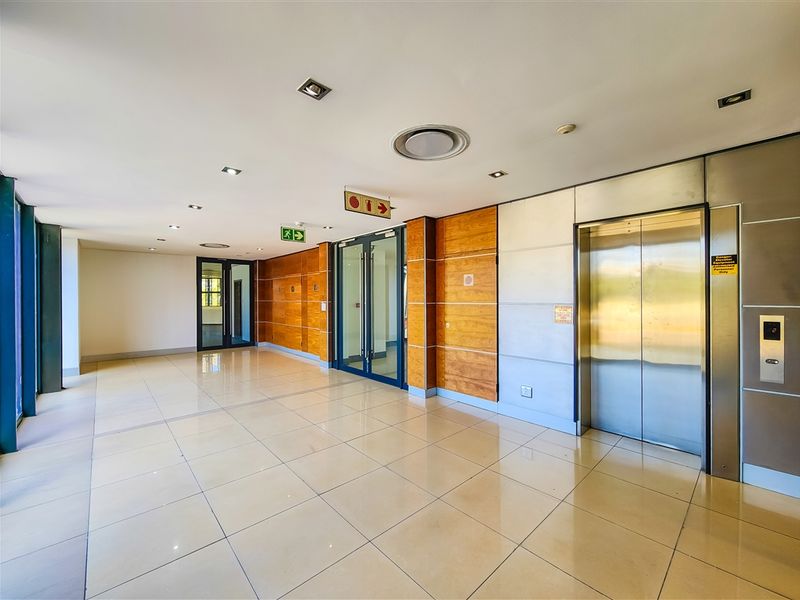 A spacious and modern office building lobby featuring tiled floors, wood-paneled walls, and a stainless steel elevator entrance.