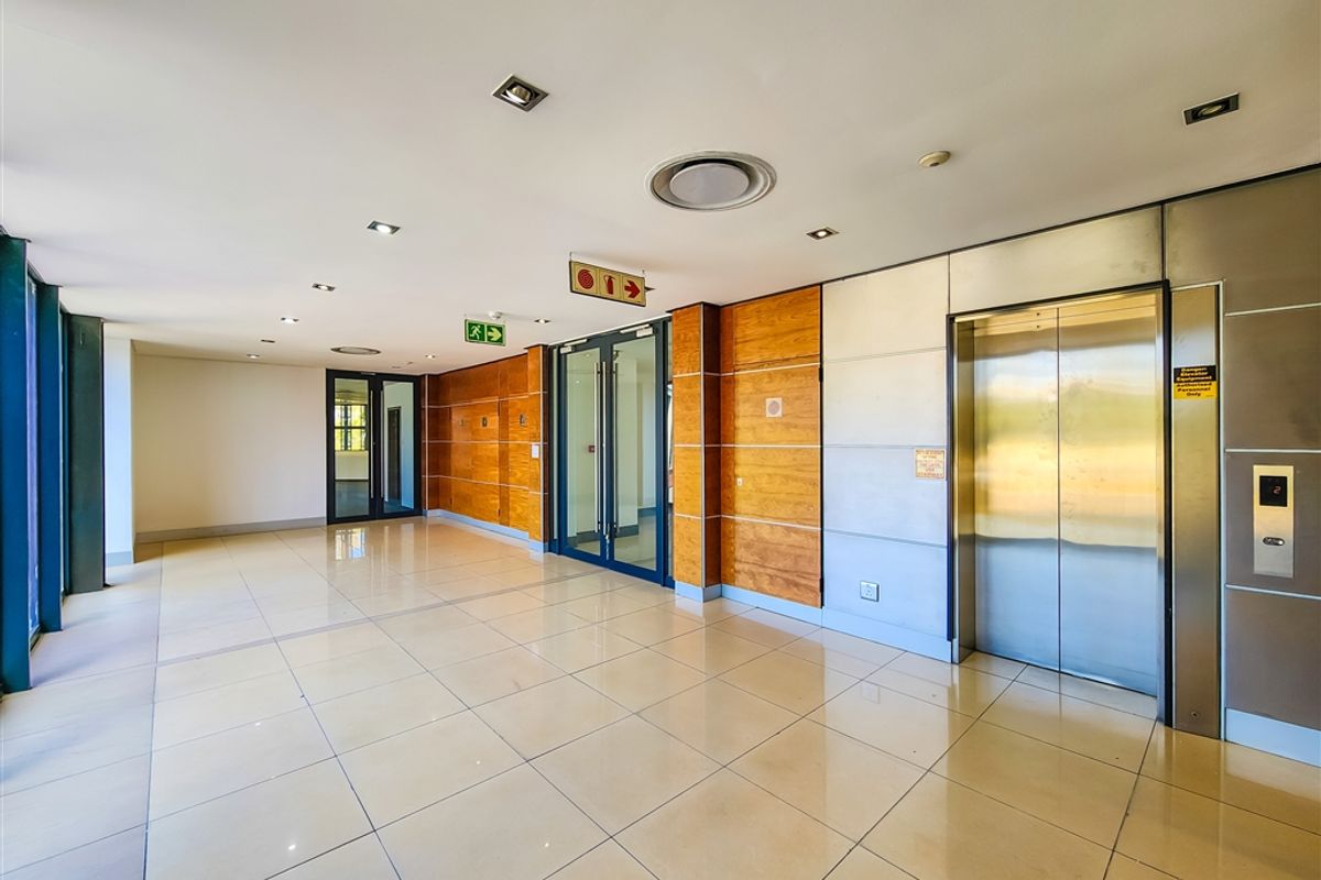 A spacious and modern office building lobby featuring tiled floors, wood-paneled walls, and a stainless steel elevator entrance.