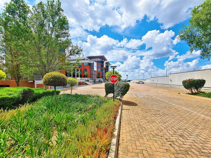 A well-maintained office park entrance featuring a paved driveway, landscaped garden beds, and clear signage leading to the main building facade.