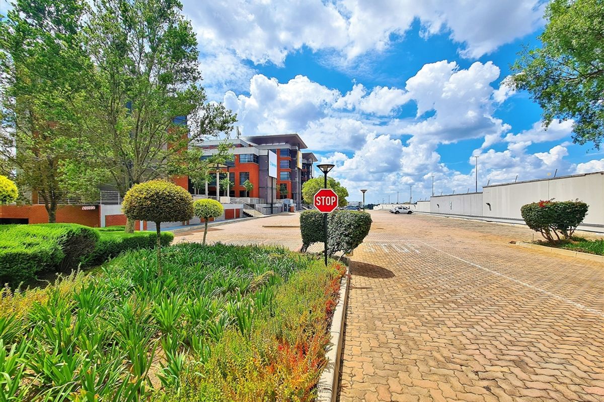 A well-maintained office park entrance featuring a paved driveway, landscaped garden beds, and clear signage leading to the main building facade.