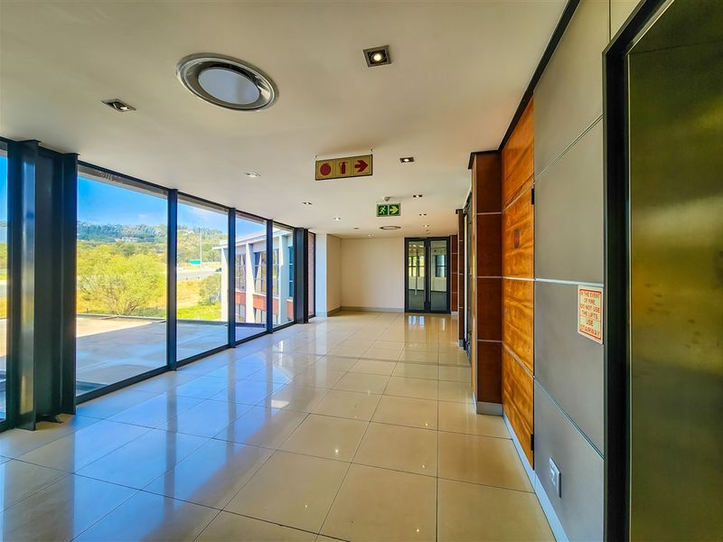 A bright, modern office hallway featuring floor-to-ceiling windows, polished ceramic tile flooring, and elegant wood veneer wall paneling.
