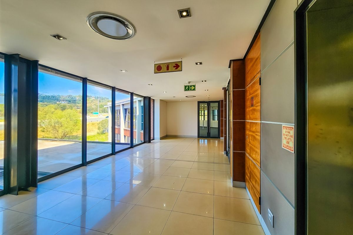 A bright, modern office hallway featuring floor-to-ceiling windows, polished ceramic tile flooring, and elegant wood veneer wall paneling.