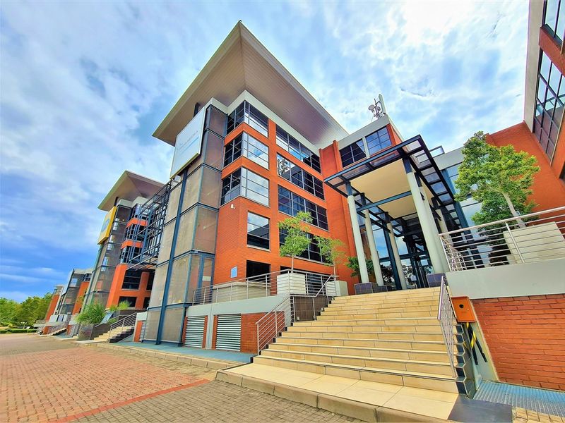 A modern multi-story office building featuring a prominent brick facade, glass curtain walls, and a grand tiled entrance staircase with stainless steel railings.