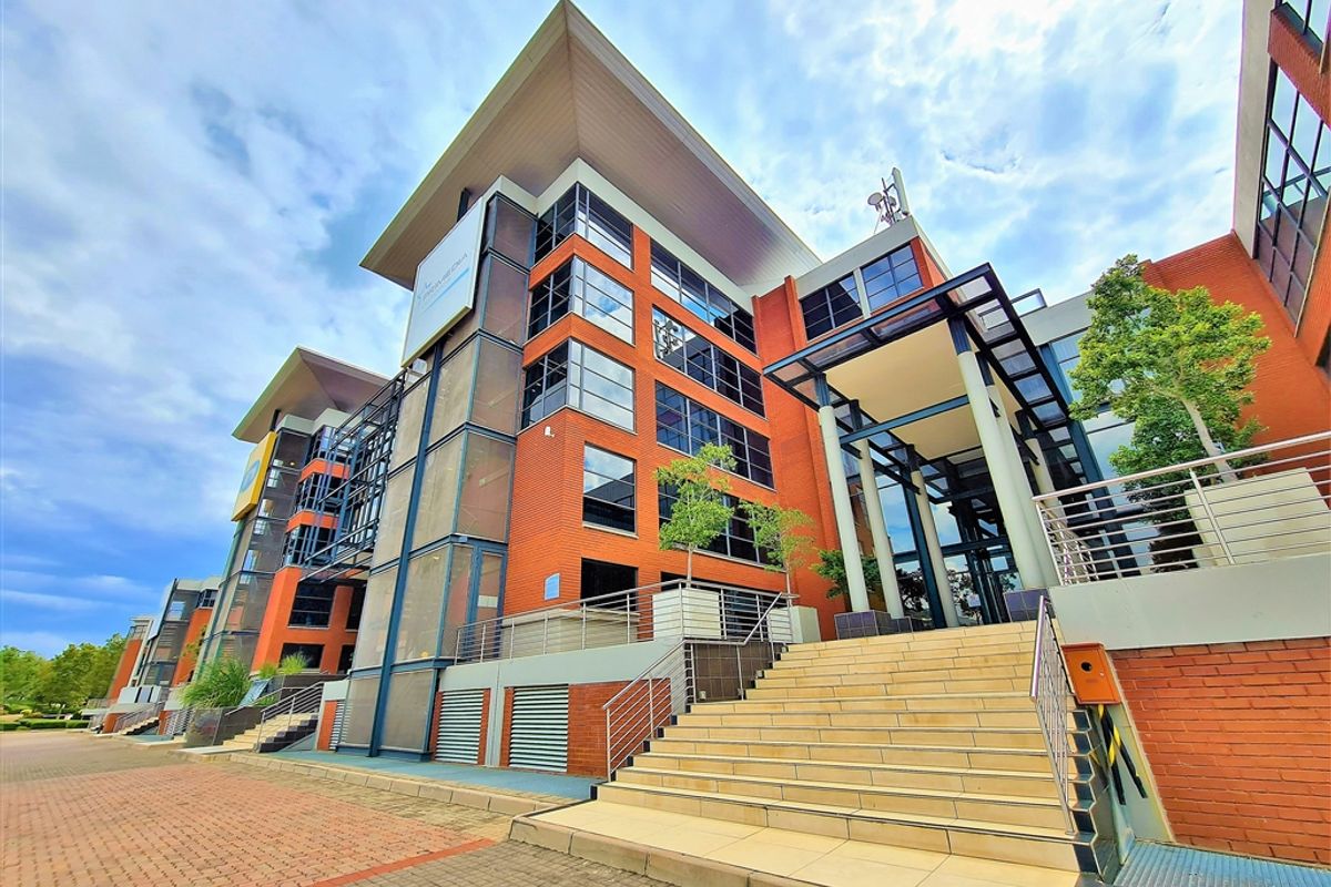 A modern multi-story office building featuring a prominent brick facade, glass curtain walls, and a grand tiled entrance staircase with stainless steel railings.