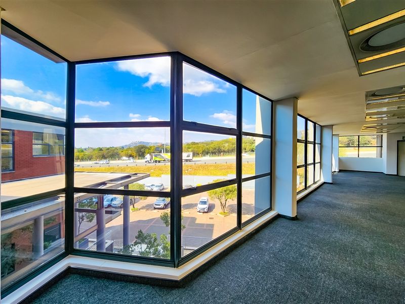 Spacious, empty office area featuring extensive floor-to-ceiling windows providing ample natural light and views of the surrounding parking and landscape.