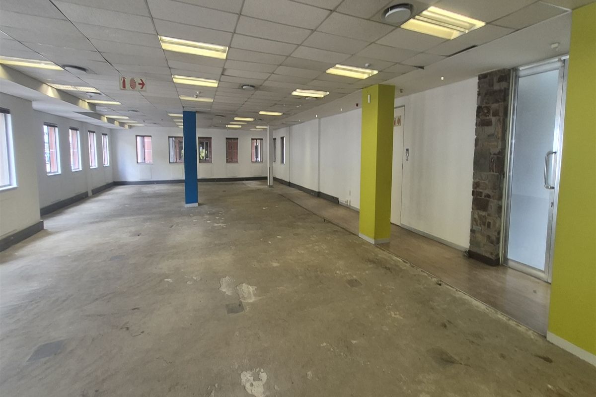 An expansive, empty open-plan office space featuring a suspended ceiling, recessed lighting, and a stone-clad pillar, currently requiring new flooring installation.