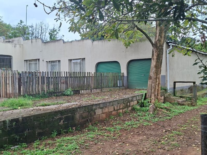Front exterior view of the property featuring a double garage with roller shutter doors, concrete driveway, and a retaining wall.
