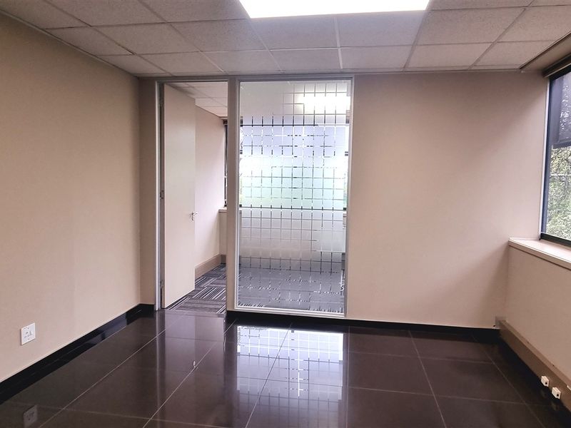 A clean, empty office space featuring dark tiled flooring, a suspended ceiling, and a glass partition wall, offering a professional and versatile work environment.