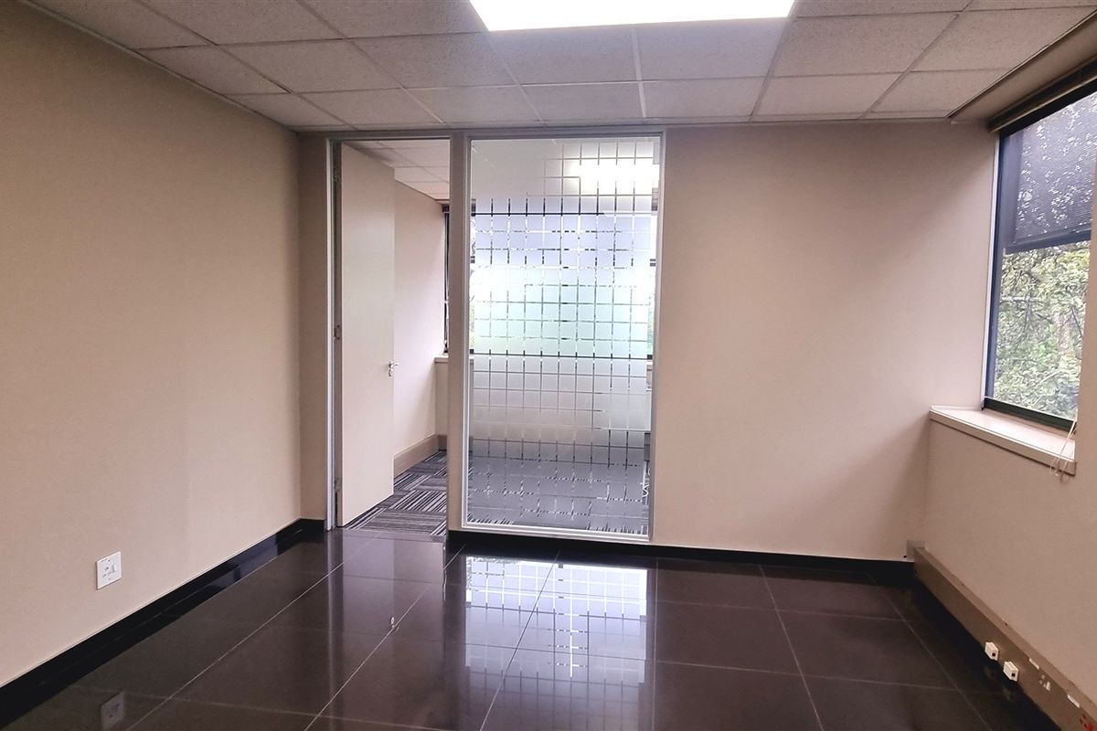 A clean, empty office space featuring dark tiled flooring, a suspended ceiling, and a glass partition wall, offering a professional and versatile work environment.