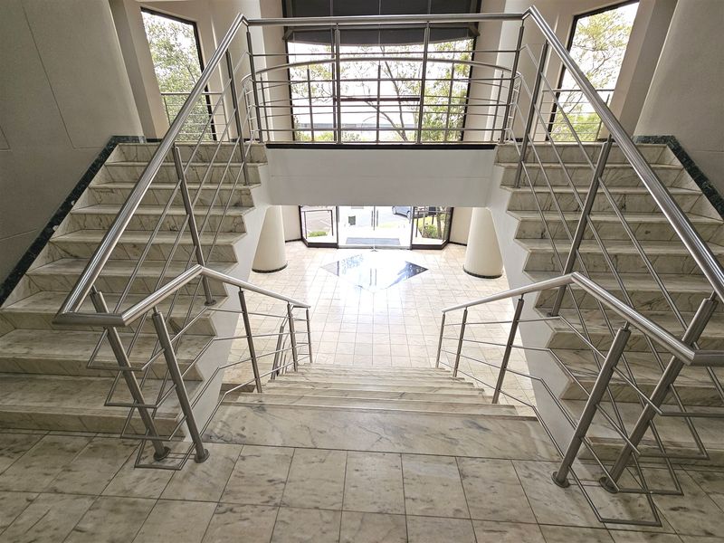 Grand office entrance featuring a symmetrical marble staircase with stainless steel balustrades and polished tile flooring leading to a glass-fronted lobby.