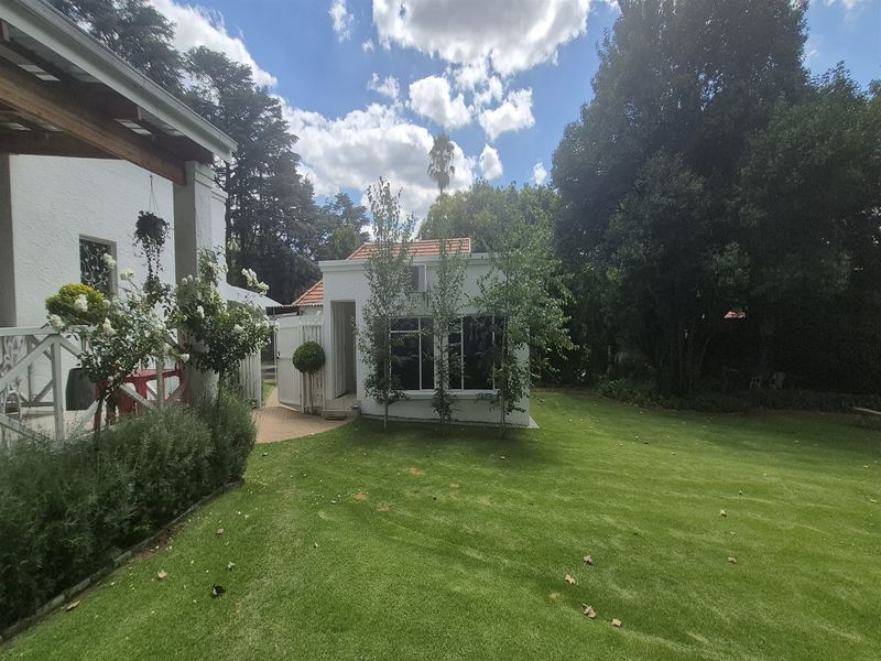 A well-maintained rear garden featuring a lush lawn, paved pathways, and a detached office structure with a tiled roof and air conditioning unit.