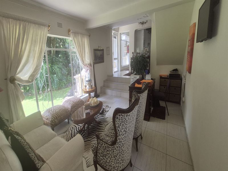 A bright office reception area featuring tiled flooring, large glass sliding doors providing garden views, and a staircase leading to upper levels.