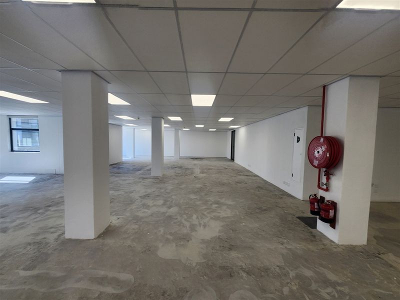 An open-plan office space featuring a suspended ceiling, recessed lighting, and exposed concrete flooring, equipped with essential fire safety infrastructure.