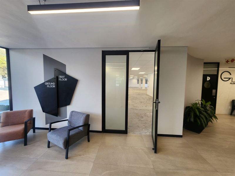 Modern office building entrance lobby featuring tiled flooring, contemporary directional signage, and a glass-panelled door leading into an open-plan office space.