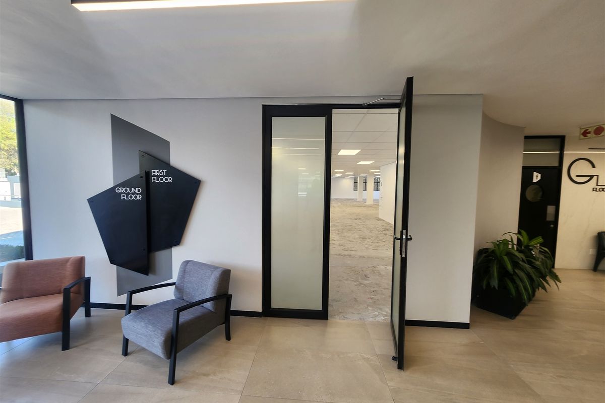 Modern office building entrance lobby featuring tiled flooring, contemporary directional signage, and a glass-panelled door leading into an open-plan office space.