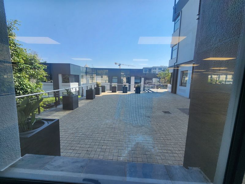 A spacious outdoor terrace featuring paved flooring and metal railings, offering an open-air area accessible from the office building.