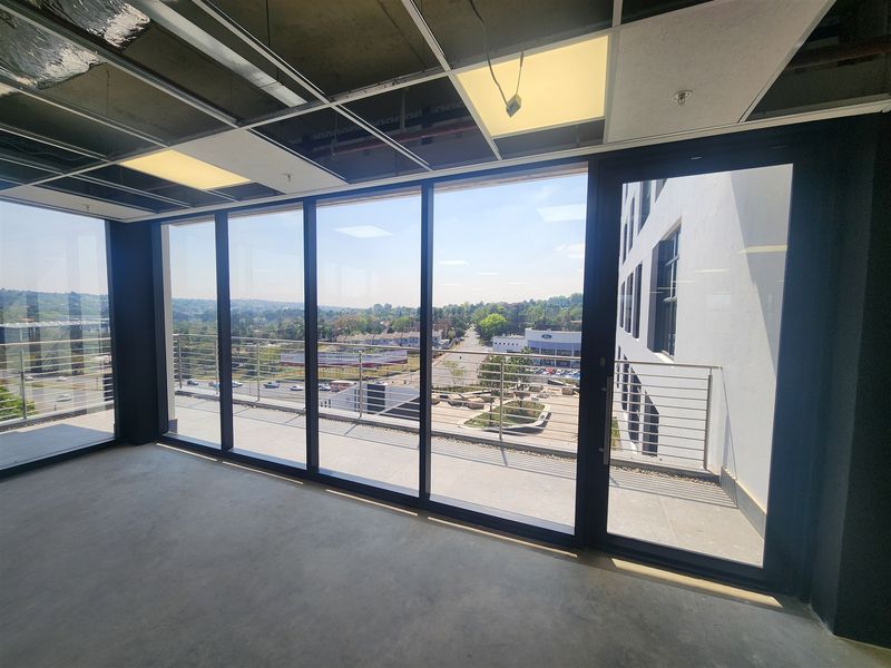 Unfinished office space featuring floor-to-ceiling windows, access to a private balcony, and an exposed ceiling grid ready for final fit-out.