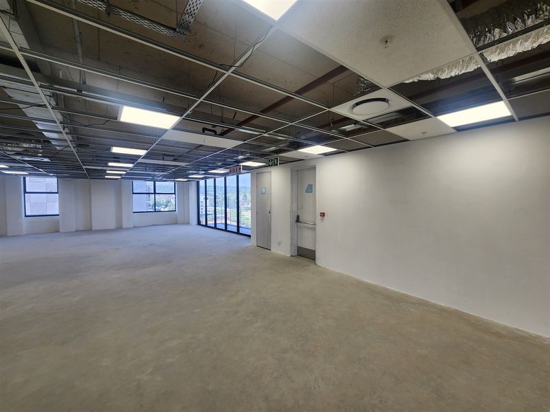 An expansive, open-plan office space featuring a raw industrial aesthetic with exposed ceiling infrastructure, concrete flooring, and large windows providing natural light.