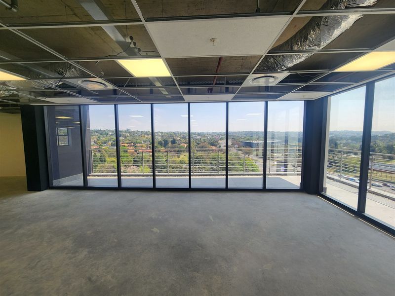 An unfinished open-plan office space featuring floor-to-ceiling windows with expansive views and access to a balcony.